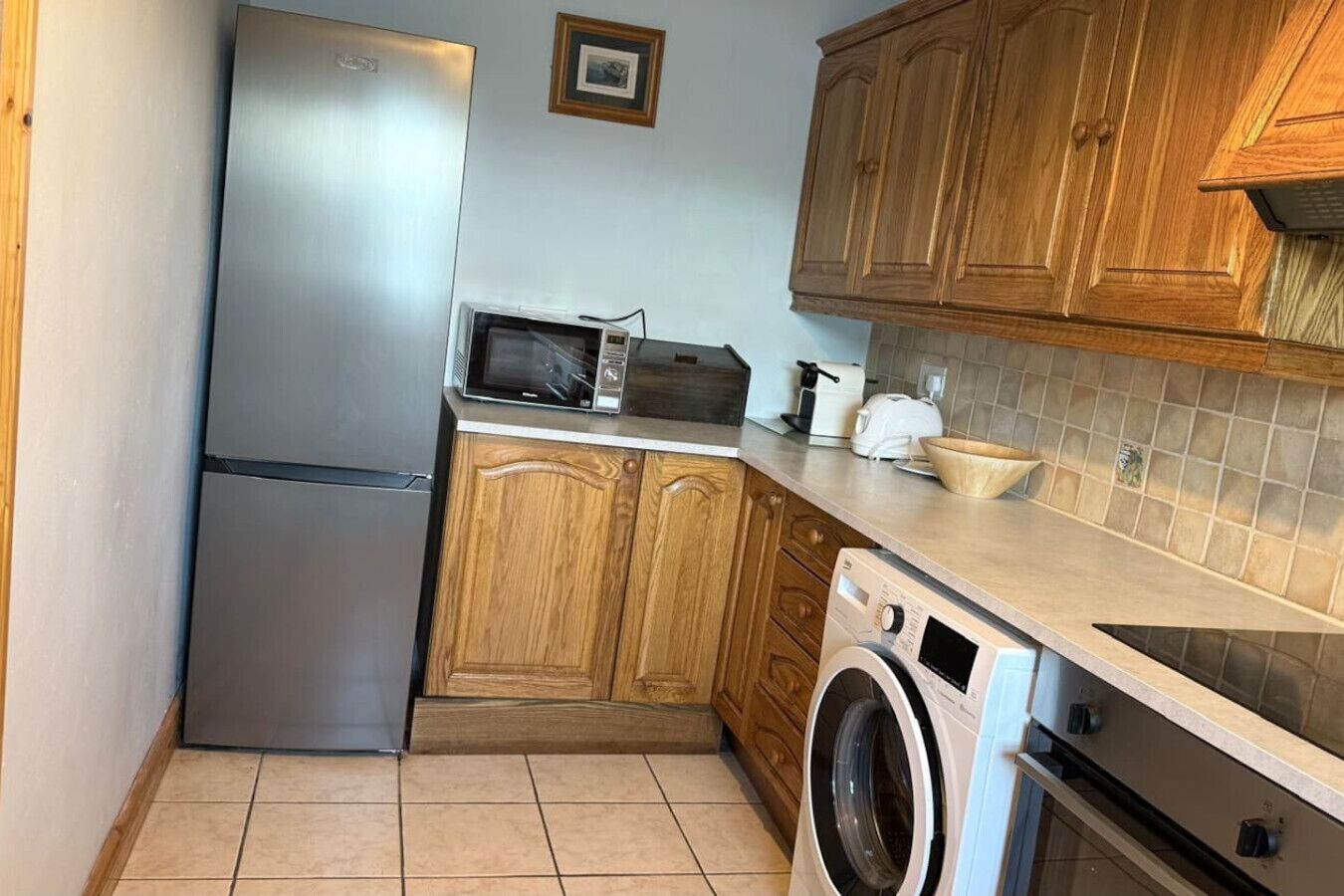 Eine kleine Küche mit Kühlschrank, Mikrowelle, Toaster und Waschmaschine.