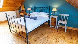 Ein Schlafzimmer mit einem Metallbettgestell, Holzboden, blauer Wand, einem kleinen Nachttisch aus Holz, einem weißen Stuhl und zwei Nachttischlampen.