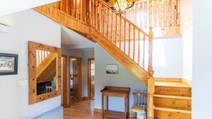 Eine Holztreppe führt zu einer oberen Etage, ein Holztisch mit einem Stuhl und ein gerahmtes Bild an der Wand.