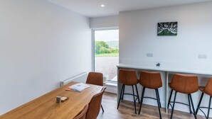 Ein moderner Essbereich mit einem Holztisch und braunen Stühlen, ein Fenster mit Blick auf Grünflächen und ein Gemälde an der Wand.