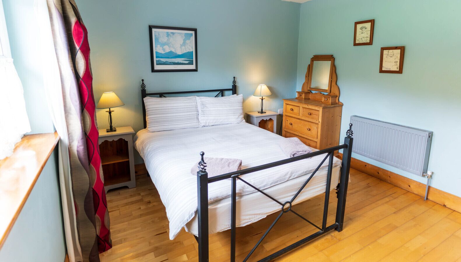 Een slaapkamer met een bed, nachtkastjes, een dressoir, een radiator en wanddecoratie.