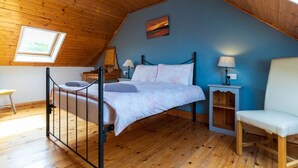 Een slaapkamer met een schuine kap, een bed, een stoel, een nachtkastje en een raam.