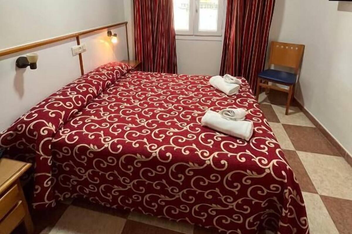 A bedroom with a bed, curtains, a chair, a TV, and a window.