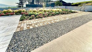 A landscaped outdoor area with a paved walkway, gravel path, and a variety of plants. - The Summit - Skellig Coast (Cahersiveen)