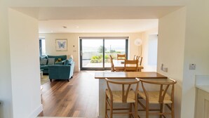 A modern living room with a sofa, a dining table with chairs, and a large sliding glass door leading to an outdoor area. - The Summit - Skellig Coast (Cahersiveen)