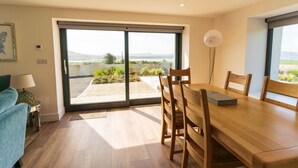 A dining area with a wooden table and chairs, a sofa, and a view through a glass door to an outdoor garden. - The Summit - Skellig Coast (Cahersiveen)