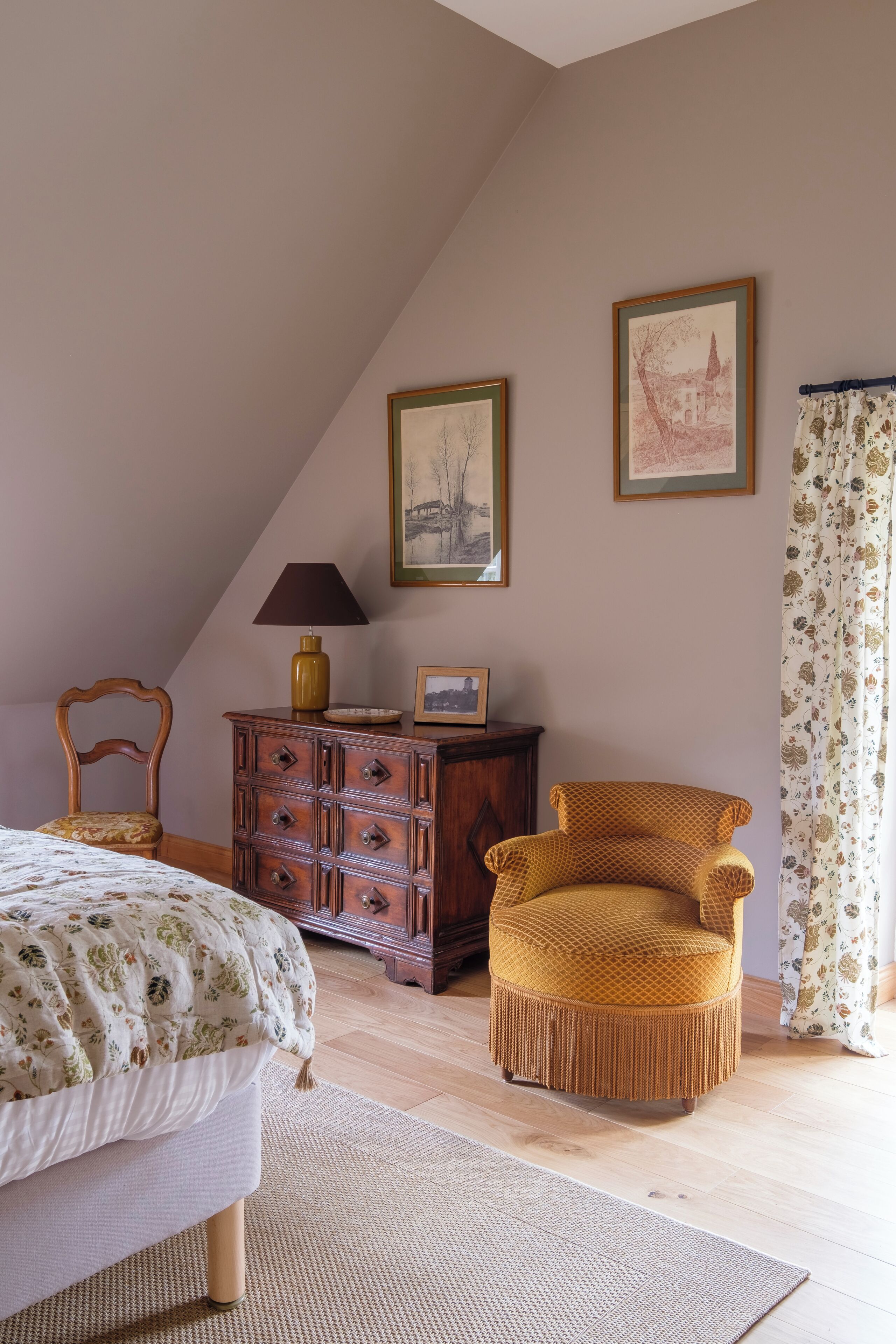 A bedroom with a bed, a wooden dresser, a chair, a lamp, and two framed pictures on the wall.
