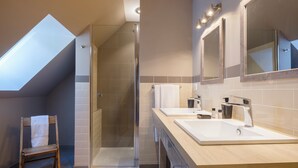 Un baño moderno con tragaluz, ducha y dos lavamanos.