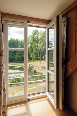 A room with a large sliding glass door leading to an outdoor area with a pond and trees. - The Prunget Estate (Tendu)