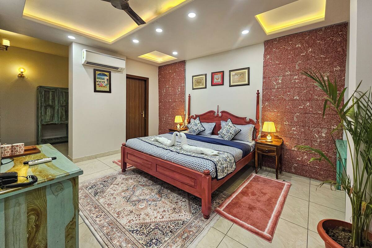 A bedroom with a bed, bedside lamps, a ceiling fan, a wall-mounted air conditioner, and a patterned rug.