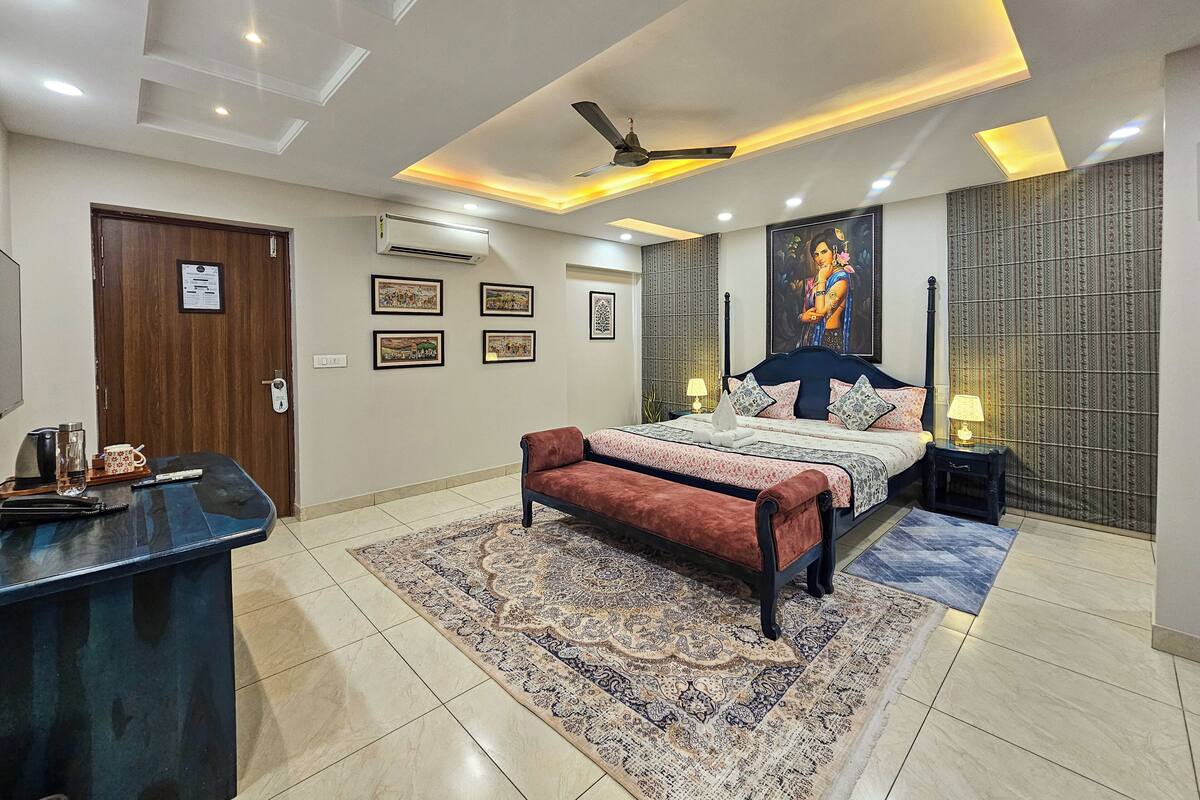 A bedroom with a bed, a desk, a ceiling fan, and a large window.
