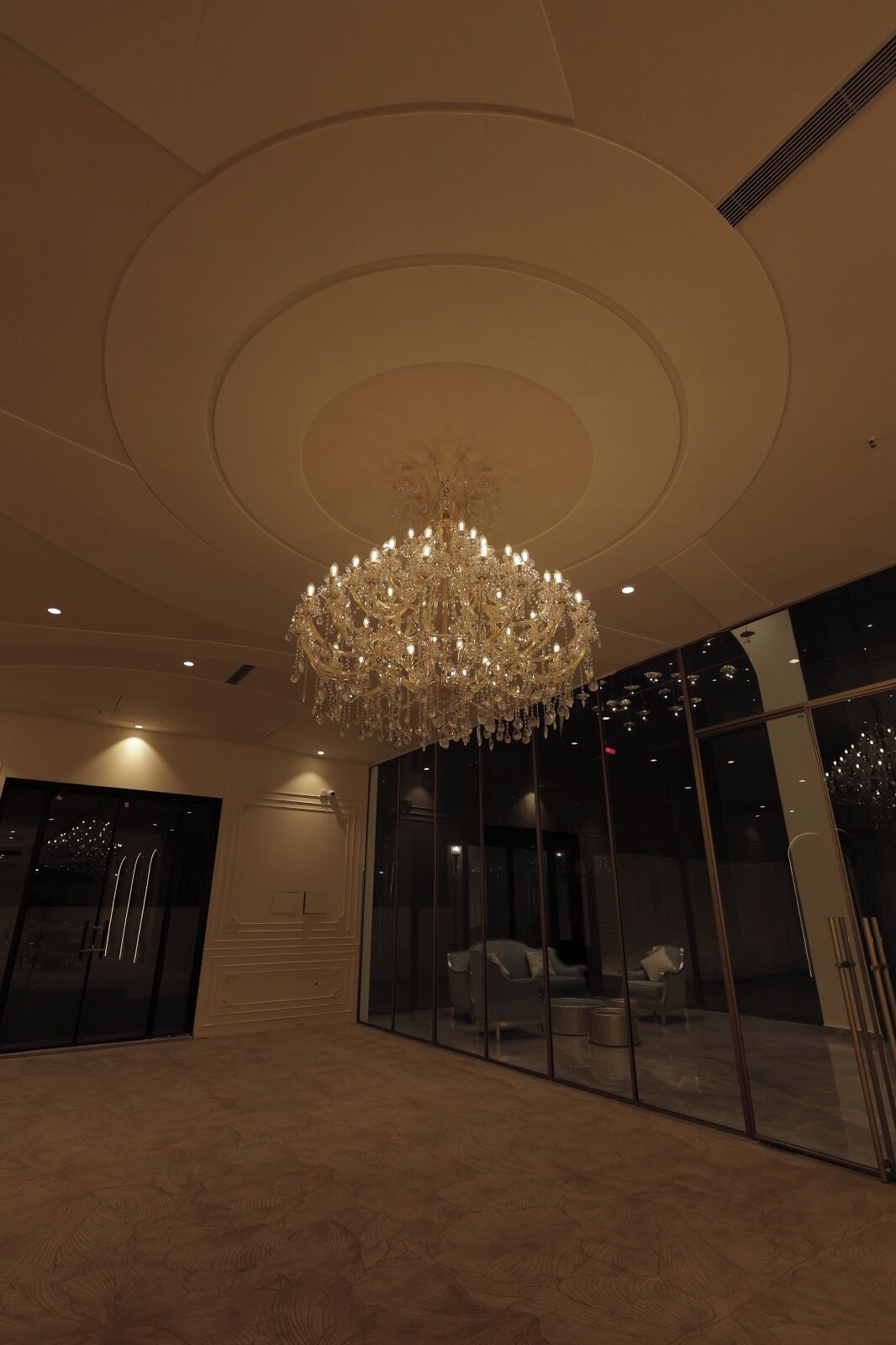A spacious lobby with a large chandelier, glass walls, and a staircase.
