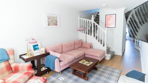 A living room with a pink sofa, a plaid rug, a wooden coffee table, a plaid armchair, and a staircase. - Hidden Gem Townhouse - Cahersiveen (Cahersiveen)