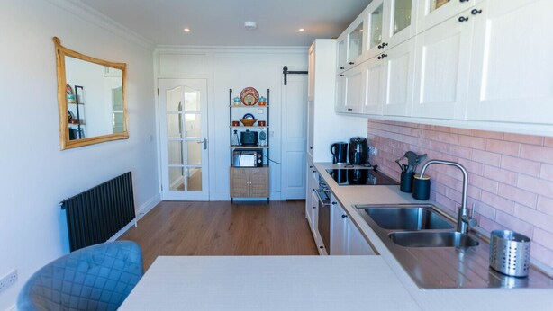 A compact kitchen with white cabinets, a built-in oven, a sink, and a microwave. - Hidden Gem Townhouse - Cahersiveen (Cahersiveen)