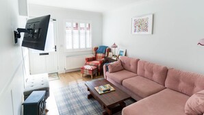 A living room with a pink sofa, a plaid rug, a coffee table with a book, a plaid armchair, and a television mounted on the wall. - Hidden Gem Townhouse - Cahersiveen (Cahersiveen)