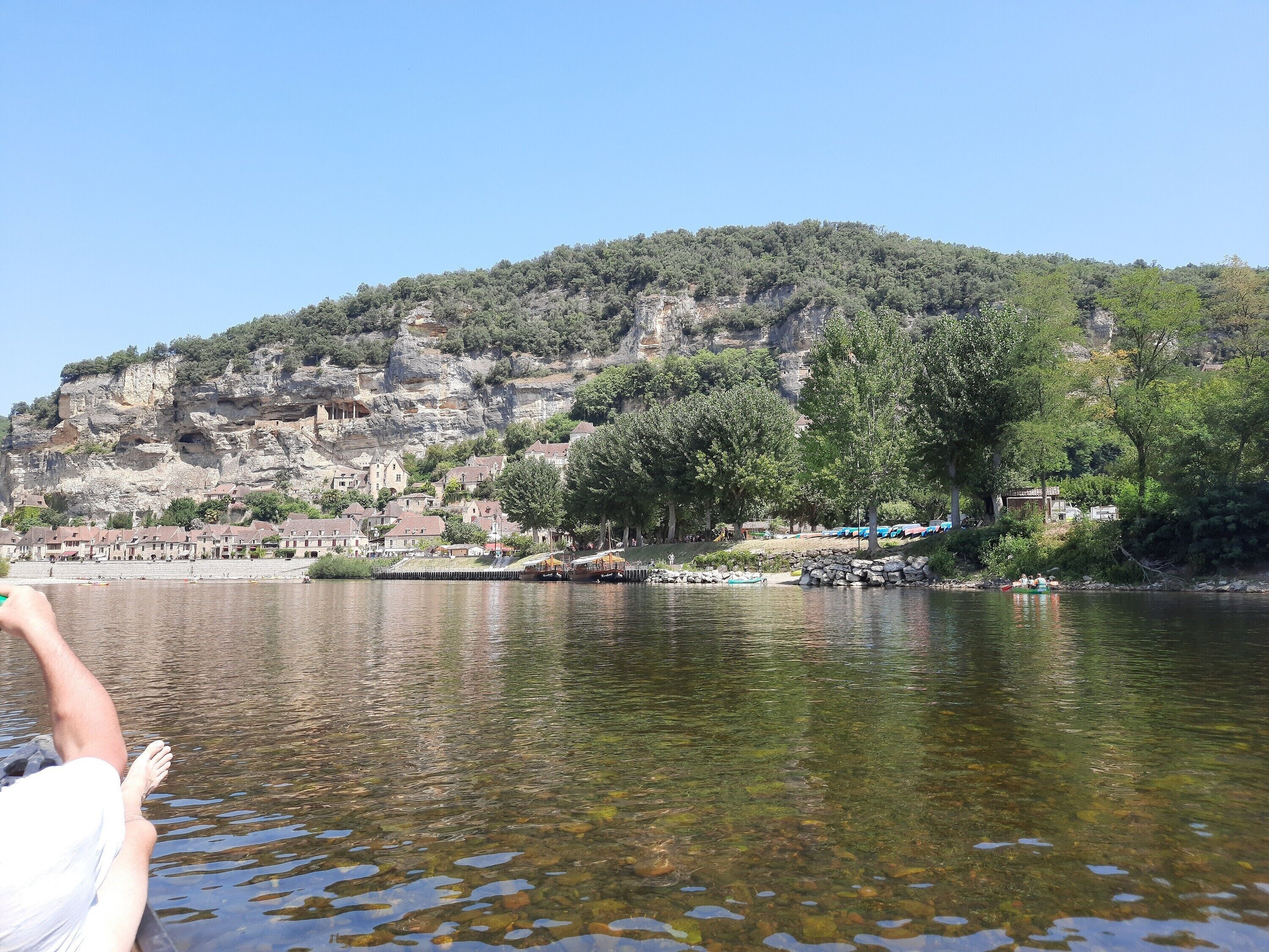 Ein Fluss mit einer felsigen Hügelkette im Hintergrund, klares Wasser und ein Boot, das am Ufer angedockt ist.