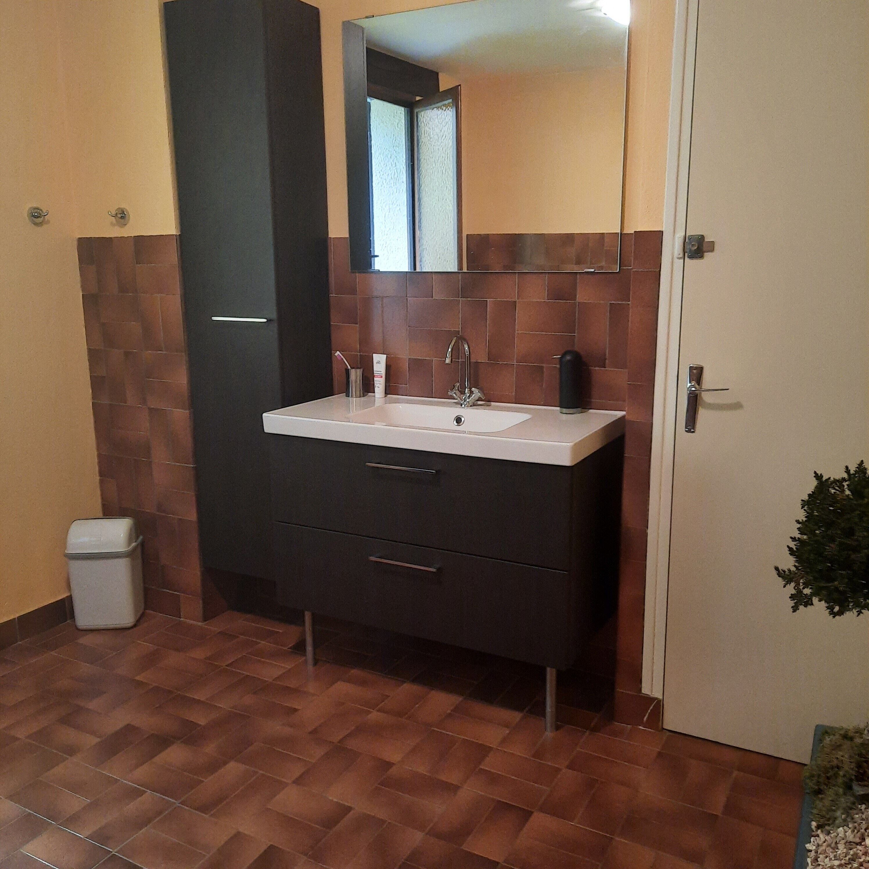 Un baño con lavamanos, espejo y un cubo de basura.
