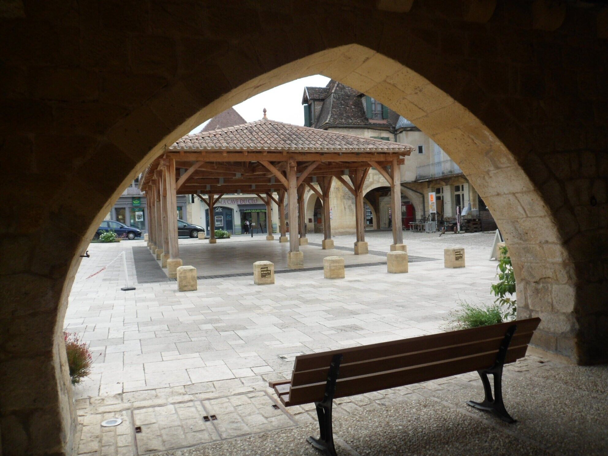 Une arche mène à une cour intérieure agrémentée d’un pavillon en bois, de bancs et de bornes en pierre.