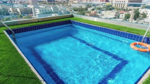 A rooftop swimming pool with clear blue water, surrounded by a tiled edge and a grassy border. - Junior King Comfort Sunday Emerald (Jeddah)