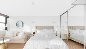 Ein Hotelzimmer mit einem großen Bett, einer Couch, einem runden Spiegel und einem Nachttisch mit Lampe.