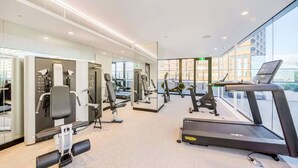 Ett modernt gym med olika typer av träningsutrustning, stora fönster och utsikt över staden.