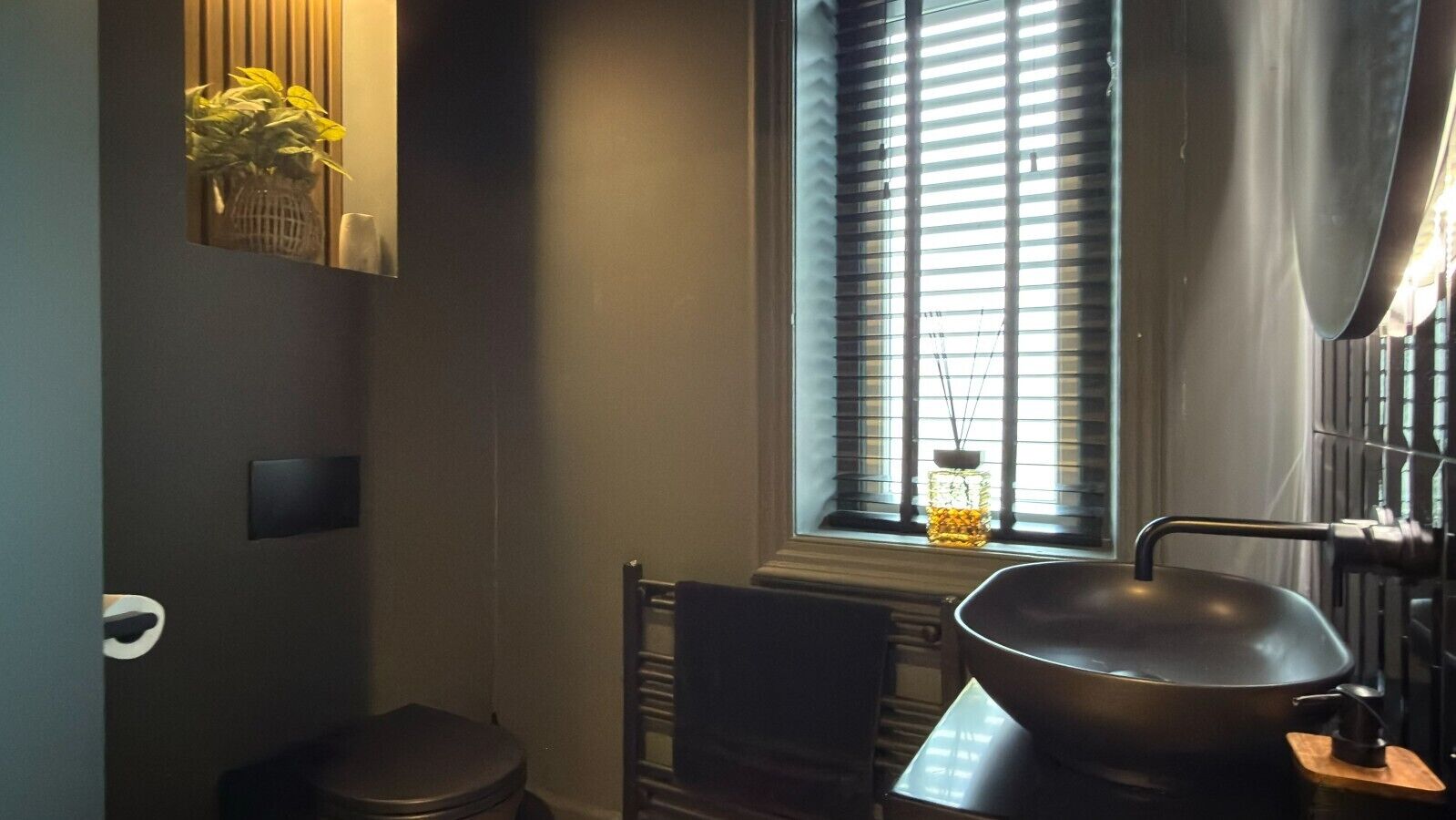 A compact bathroom with a toilet, a sink, and a window with blinds.