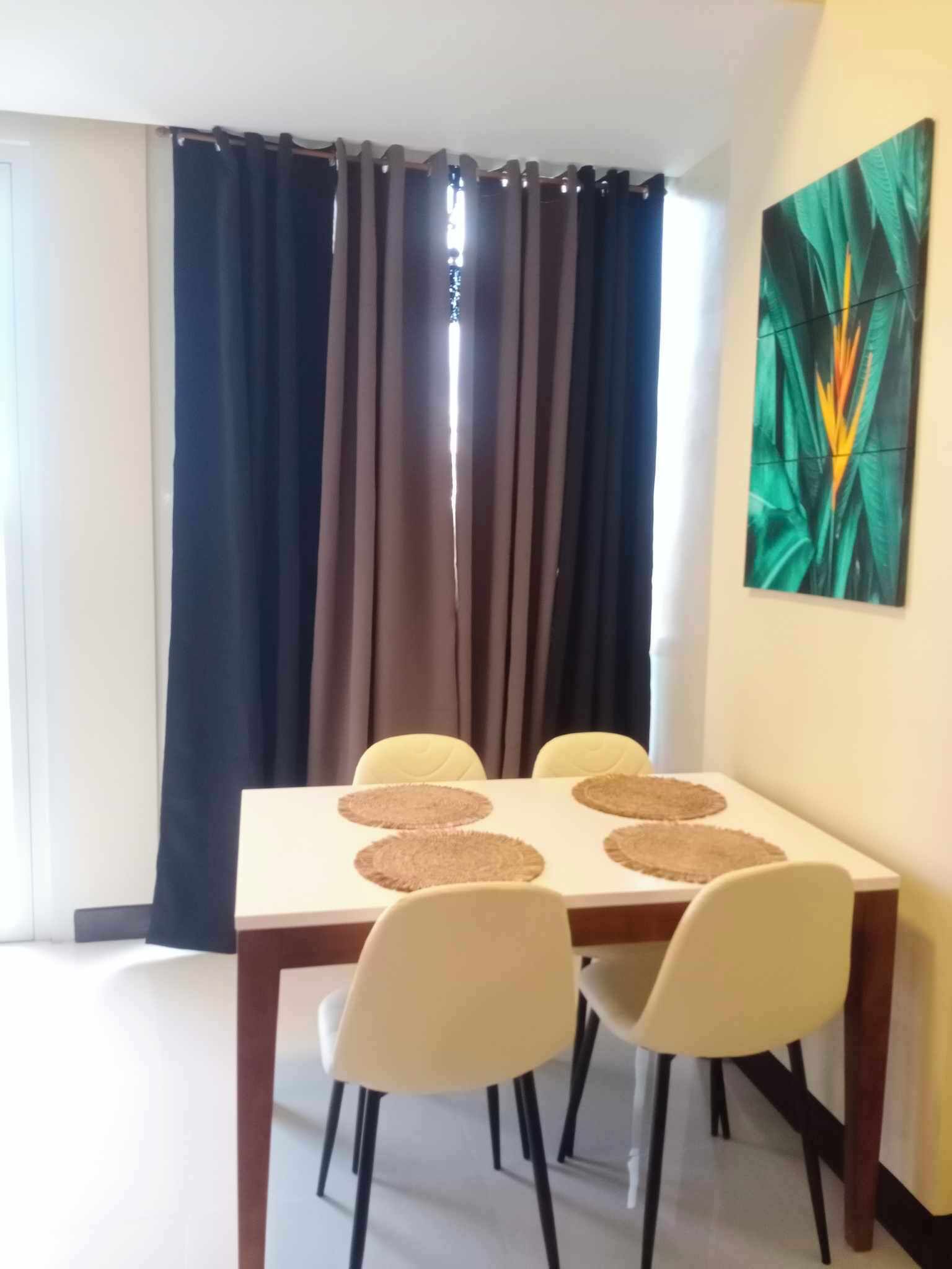A dining area with a table, four chairs, and a large window with curtains.