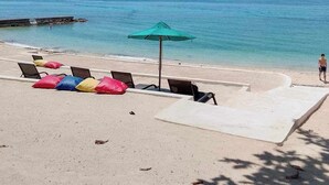 Uma praia com cadeiras de praia e um guarda-sol, céu claro e mar calmo.