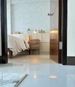 A bedroom with a bed, bedside table, lamp, and a patterned wall. - Zion Property Mactan Newtown Condo (Lapu-Lapu)