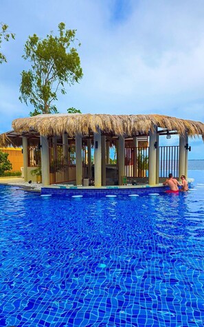 A pool area with a thatched-roof structure, clear blue water, and a view of the sea. - Zion Property Mactan Newtown Condo (Lapu-Lapu)