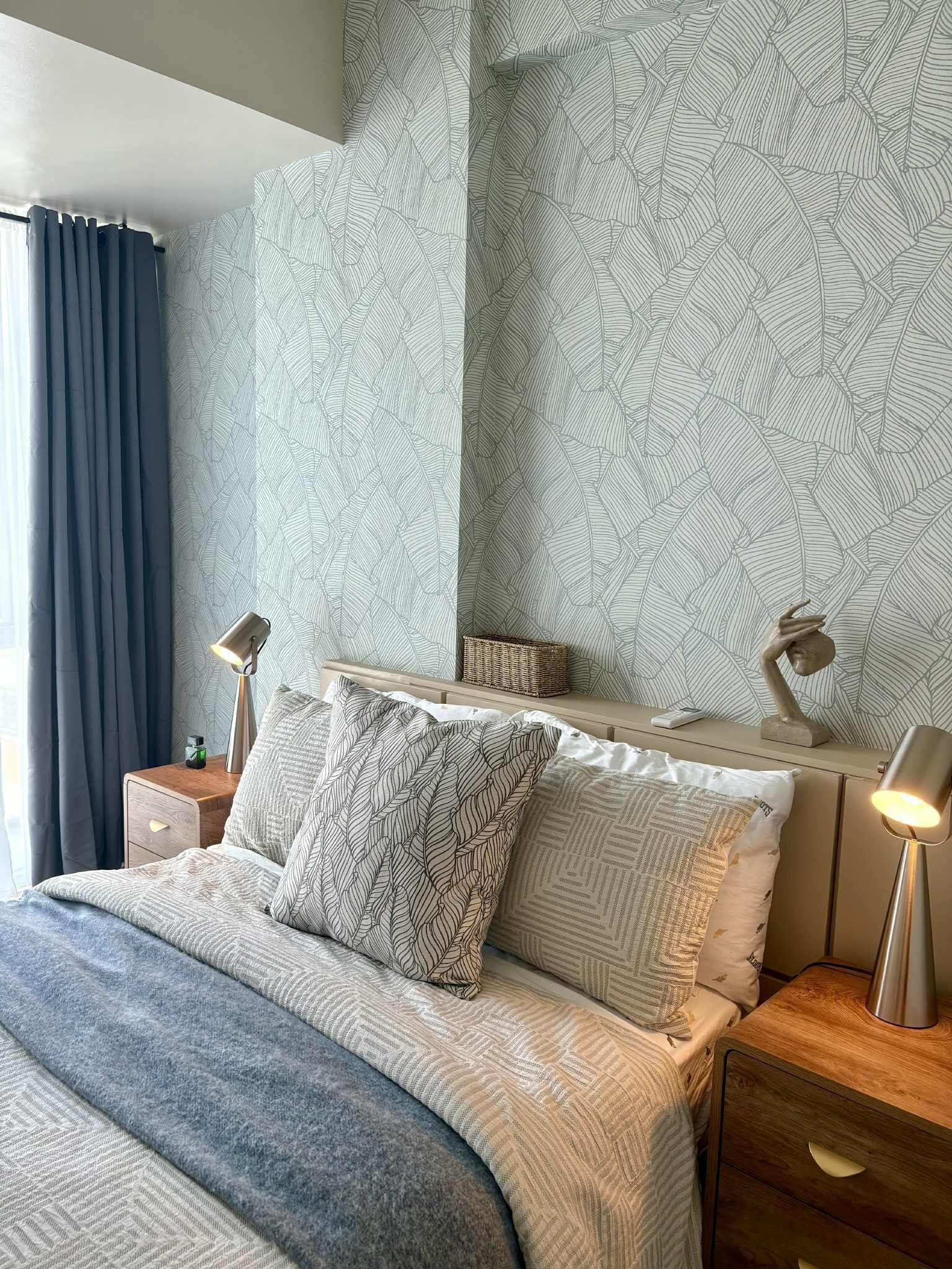 A modern bedroom with a large bed, two bedside tables, a nightstand, a lamp, and a decorative wall panel.