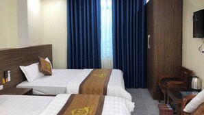 A hotel room with two beds, a wooden wardrobe, a desk with a kettle, and a television on the wall.