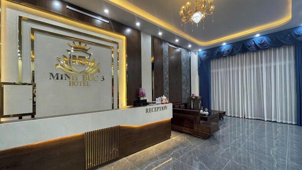 A hotel reception area with a reception desk, a chandelier, and a large mirror.