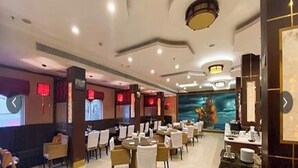 Un comedor amplio con mesas y sillas redondas, iluminación empotrada en el techo y un gran mural en la pared.