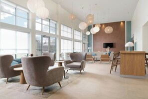 Eine geräumige Lobby mit großen Fenstern, modernen Möbeln und Pendelleuchten.