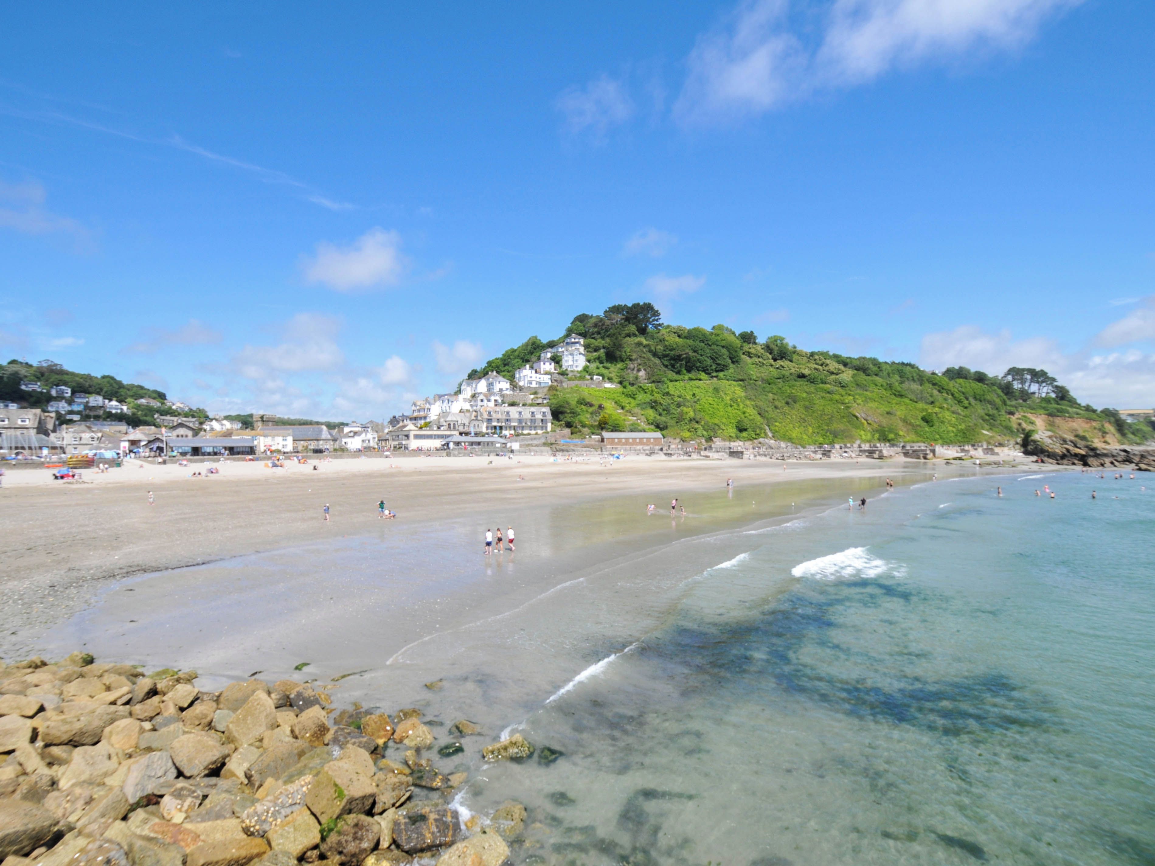 Uma praia com águas cristalinas, costa rochosa e edifícios ao fundo.