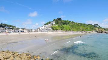 Uma praia com águas cristalinas, costa rochosa e edifícios ao fundo.