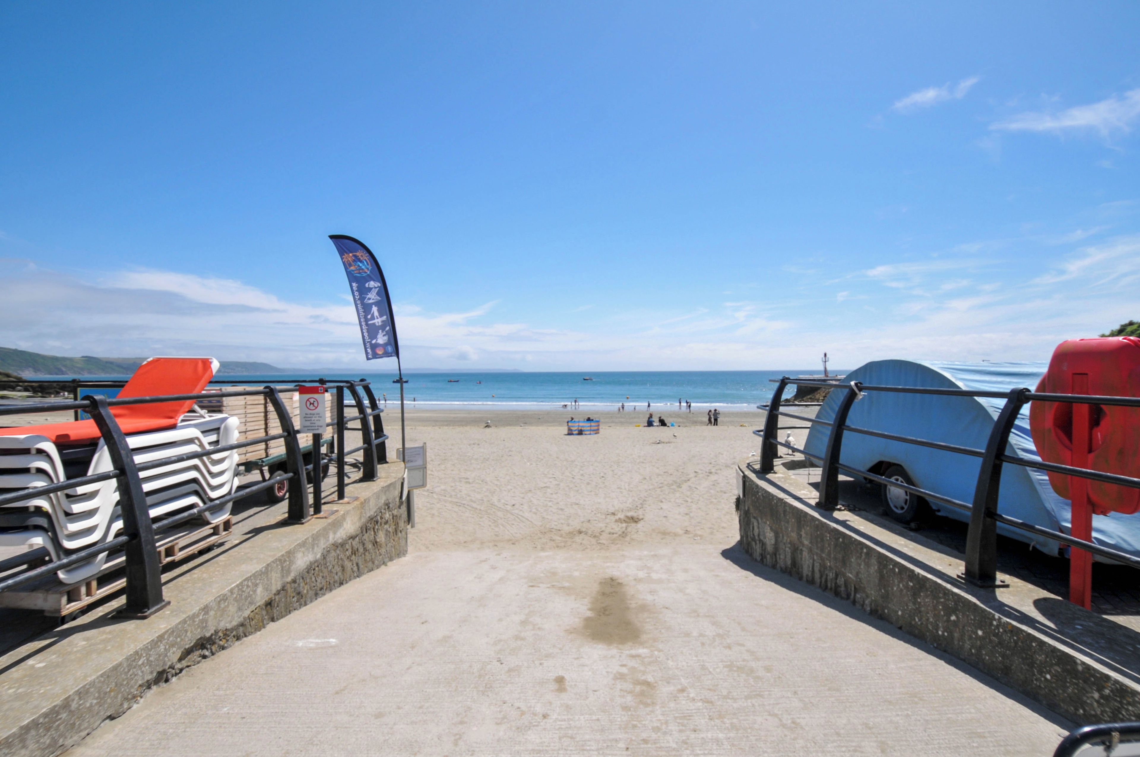 Une promenade en bord de mer qui mène à la plage, avec des chaises de plage et une bouée de sauvetage sur la droite.