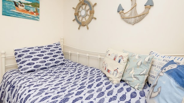 Un lit avec une couvre-lit à motifs de poissons bleus et blancs, une décoration murale sur le thème de la marine, et un tableau représentant un bateau accroché au mur.