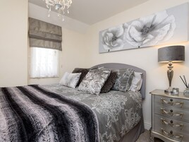 Un dormitorio con cama, mesita de noche, lámpara y un cuadro grande con motivos florales en la pared.