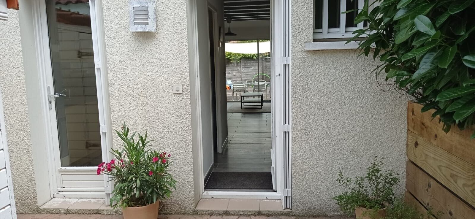 A building entrance with a sliding glass door, a potted plant with pink flowers, and a wooden fence.