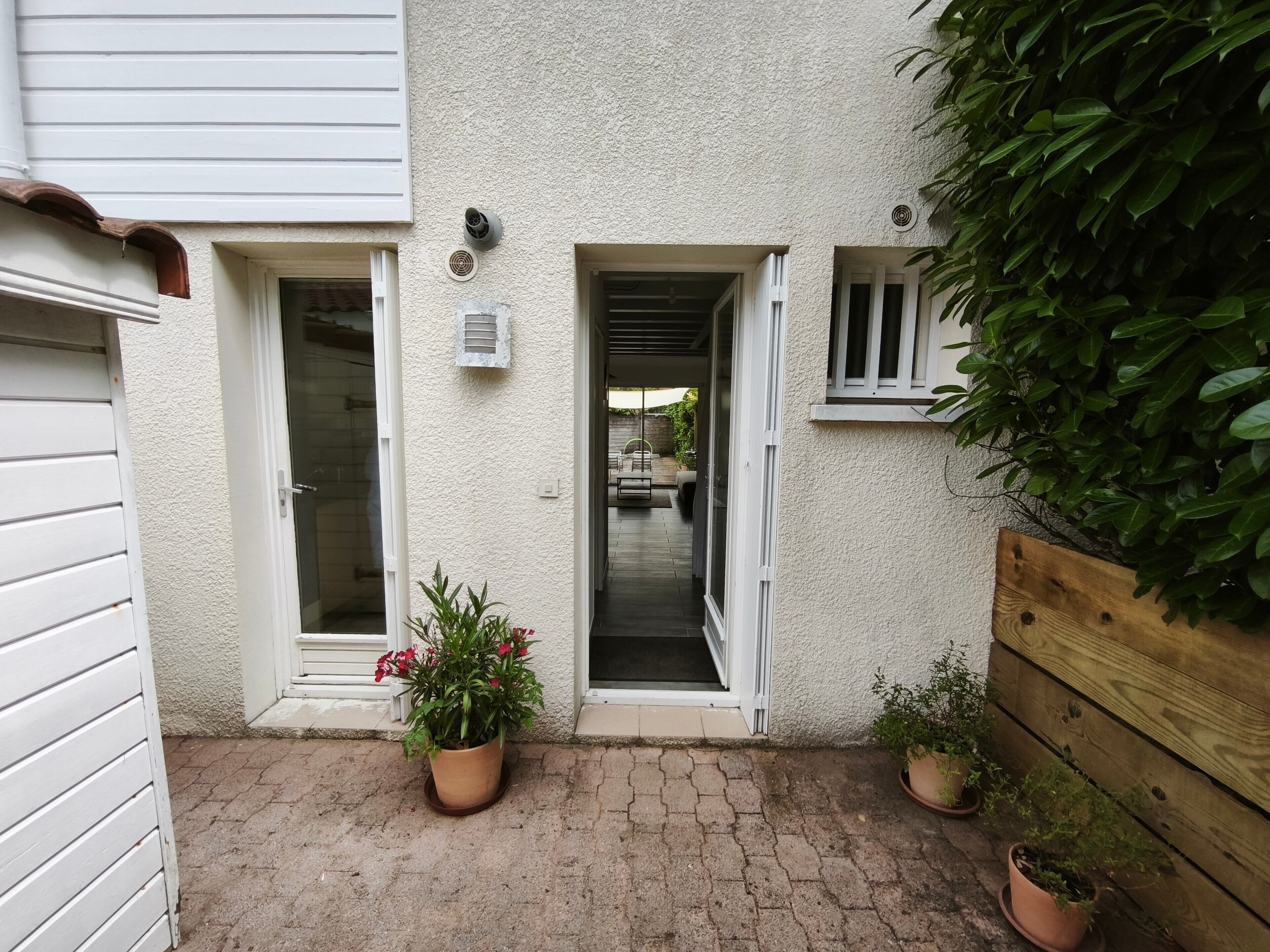 A courtyard with a white exterior wall, a wooden fence, and potted plants.