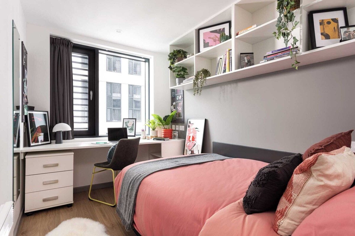 A bedroom with a bed, a desk, a chair, a bookshelf, and a window.