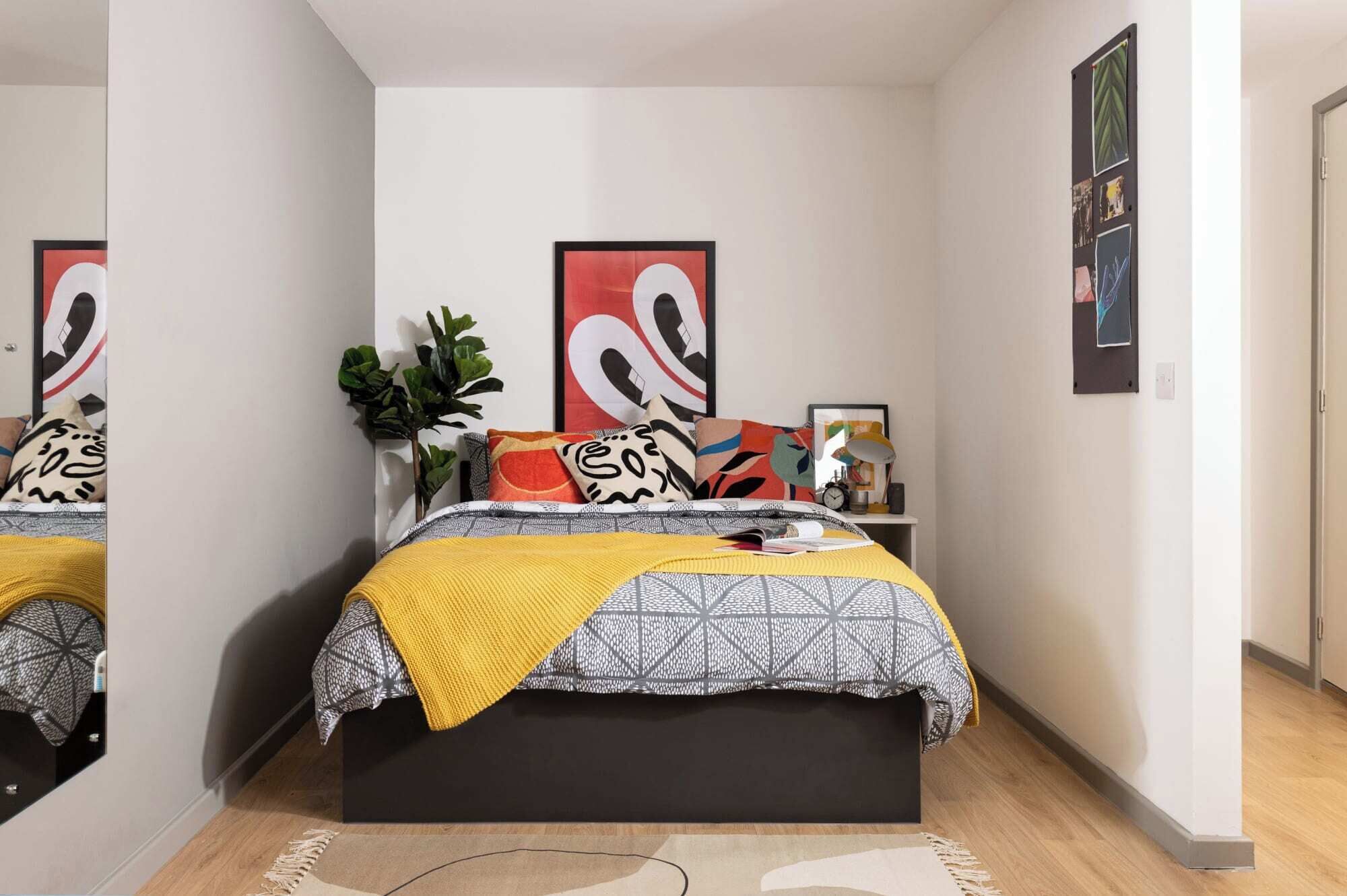 A bedroom with a bed, a bedside table, a lamp, and a wall with artwork.
