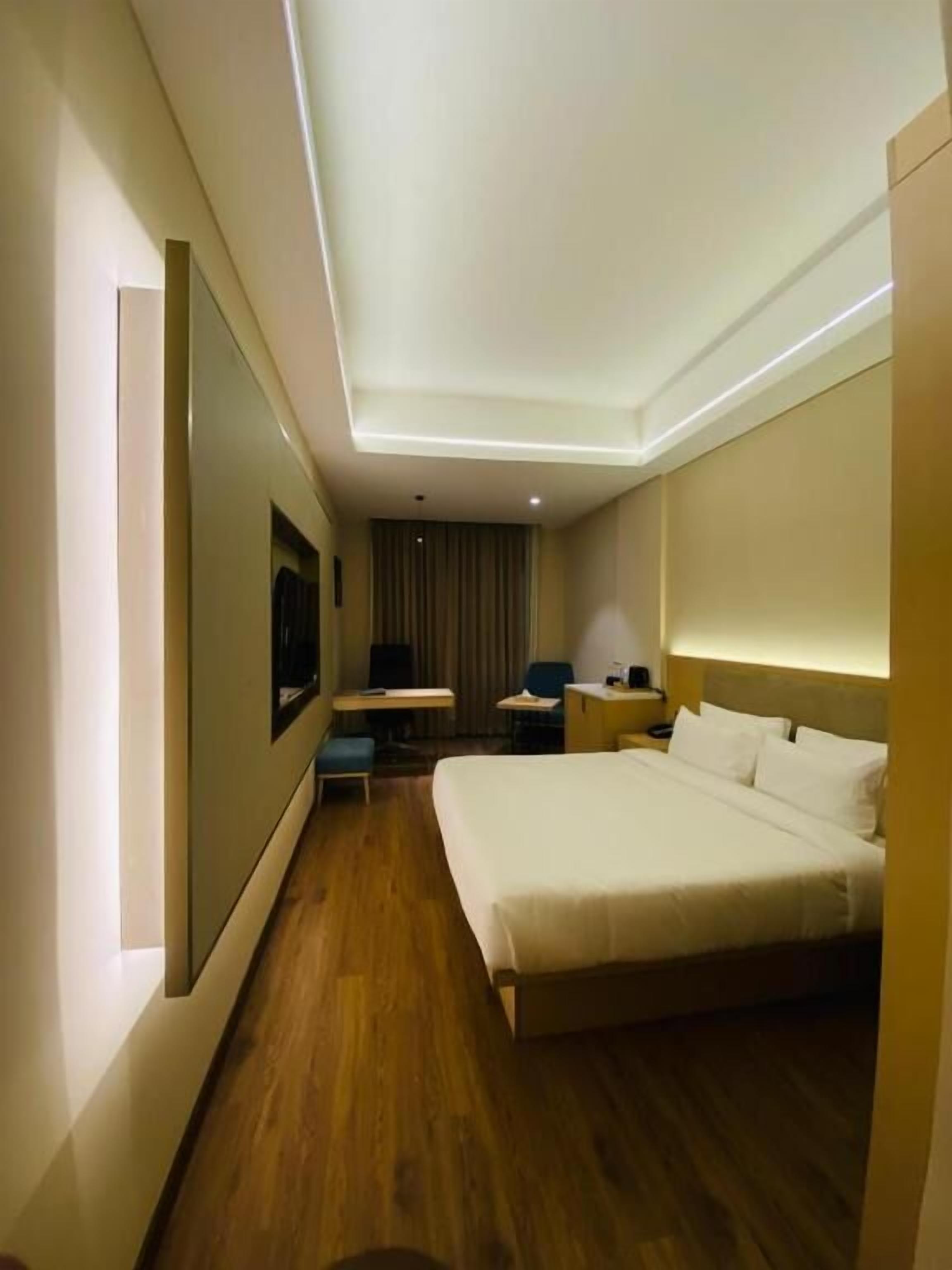 A hotel room with a bed, bedside table, lamp, desk, chair, and a flat-screen TV.