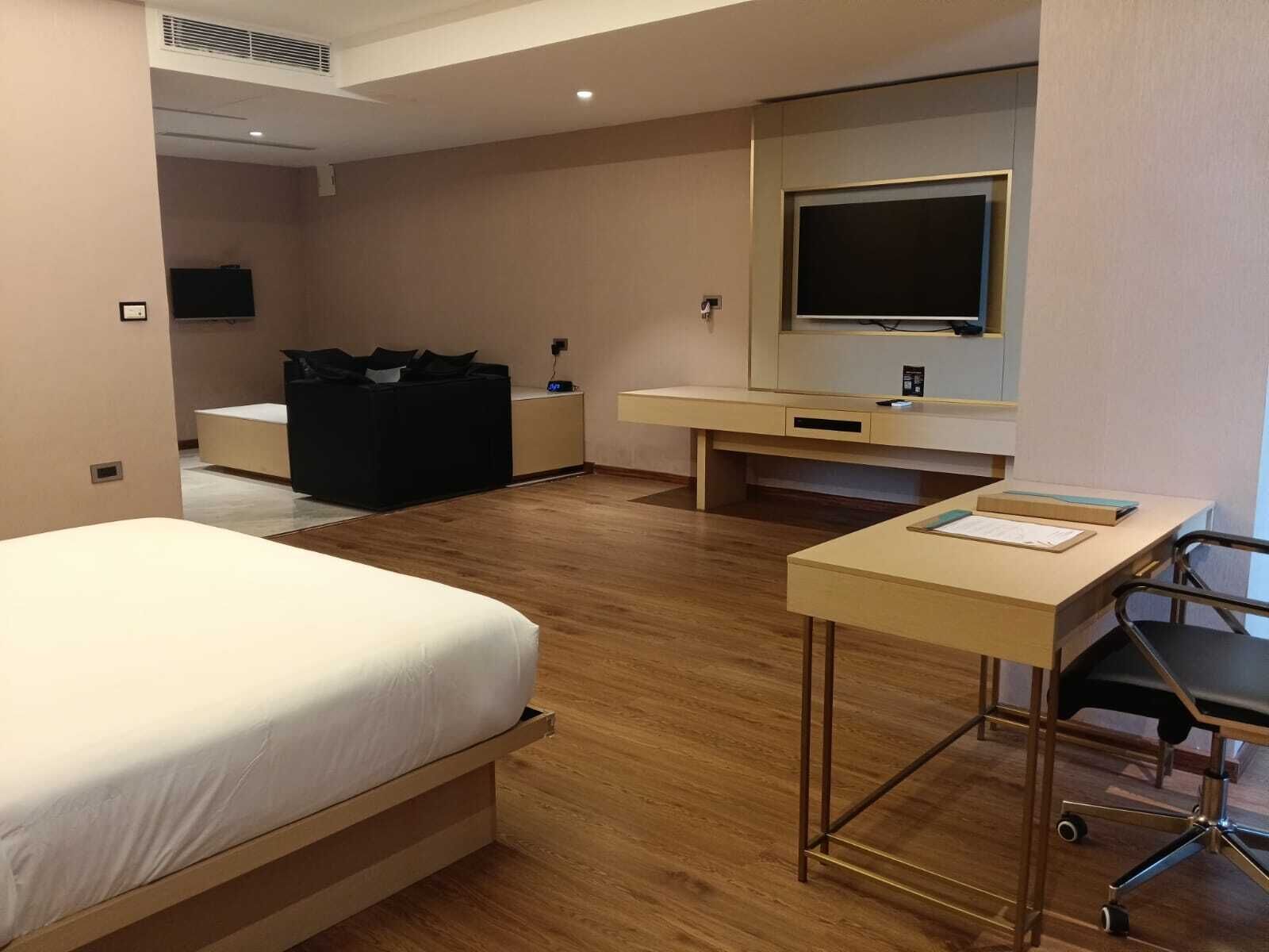 A hotel room with a bed, desk, chair, TV, and a small seating area.