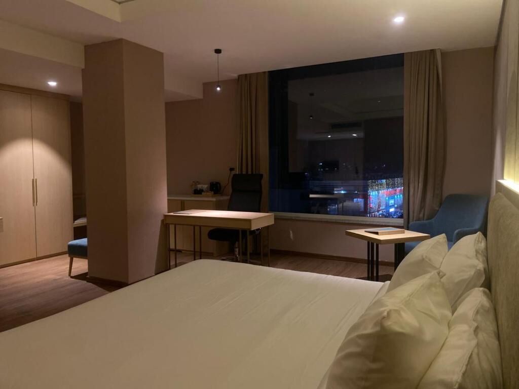 A hotel room with a bed, a desk, a chair, a window with a city view, and a wardrobe.