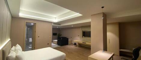 Una habitación de hotel moderna con cama, escritorio, silla, televisión y una pequeña zona de estar.