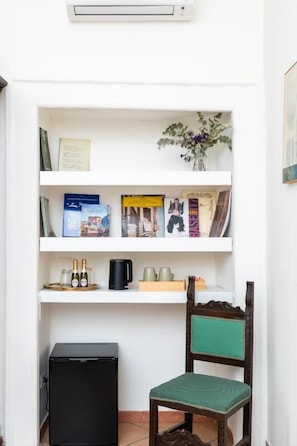 A small room with a white bookshelf, a green chair, a black heater, and a small black appliance. - Dimora dei marchesi (Naples)