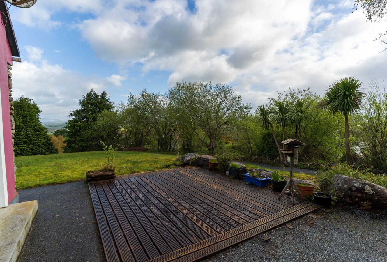 A wooden deck with a gravel path leading to a building, surrounded by greenery and trees.